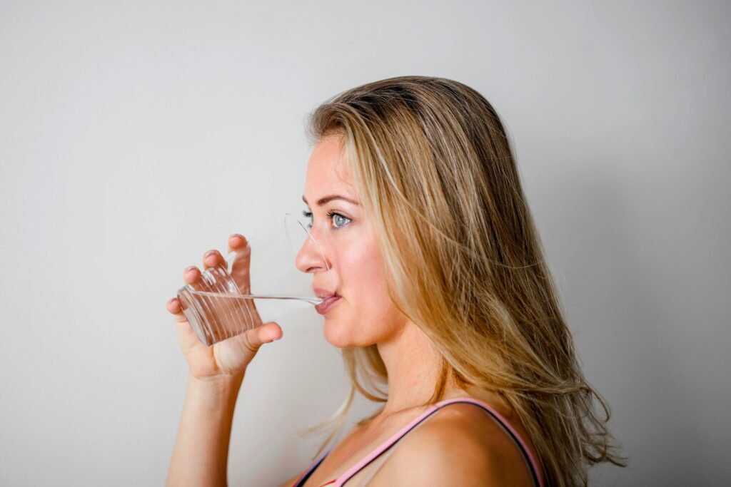 About Us magh Side view of a woman with blonde hair drinking water from a clear glass.
