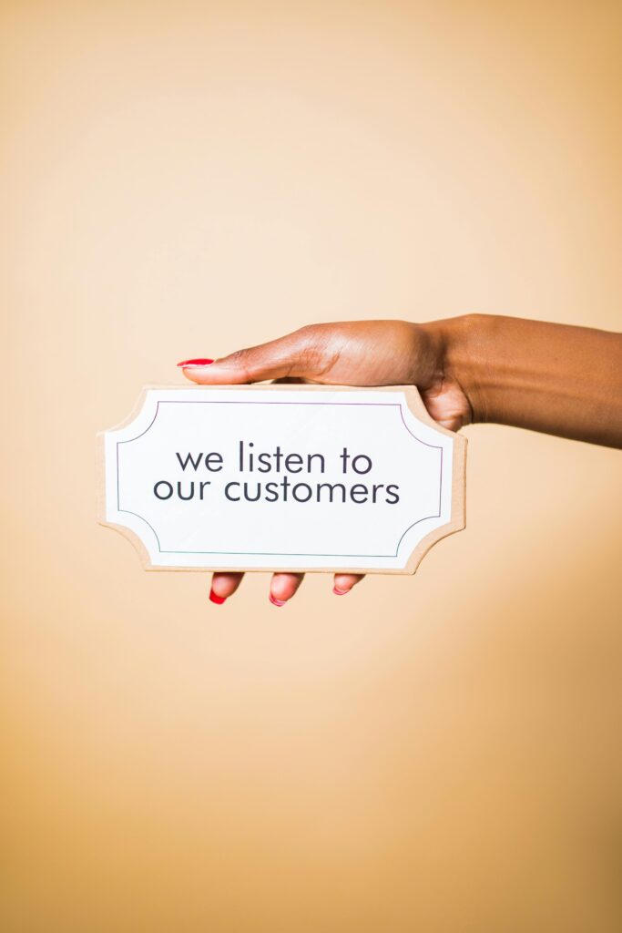 pexels photo 7564196 7564196 A hand holding a sign saying 'we listen to our customers' on a neutral background.