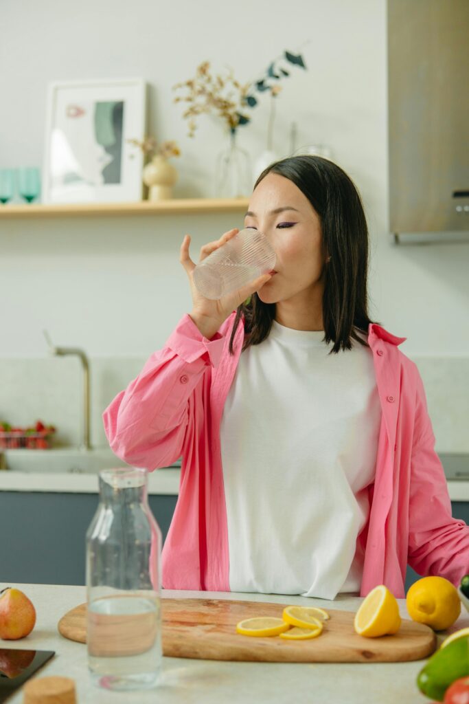 pexels photo 8845437 8845437 Asian woman in a pink overshirt drinks water in a kitchen setting promoting healthy lifestyle.